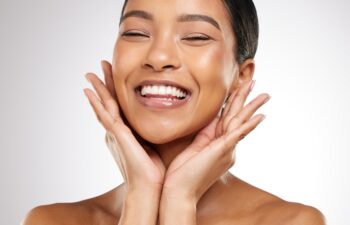 Skincare, beauty and woman with hands on face, smile and benefits of cosmetics in studio. Healthy, dermatology and girl with natural makeup for glow on skin and self care portrait on white background