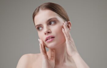 Beauty, health, cosmetics, anti-aging therapy and skin care concept - young beautiful brunette Caucasian woman touching face and looking at camera