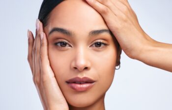 Portrait, model girl and hands on face in studio for skincare, dermatology and glow. Beauty, woman and confidence or pride for cosmetics and wellness by white background for foundation and aesthetics