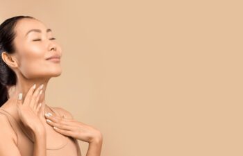 Middle aged Asian woman with closed eyes gently touching her neck, expressing satisfaction with her skin's condition, studio shot with a beige background, copy space