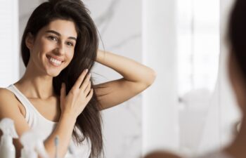 Happy young woman touching her hair and smiling looking in mirror. Home haircare concept