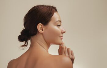 Side profile portrait of a young Caucasian woman with glowing, smooth skin, gently touching her chin. Ideal for skincare, beauty, and wellness concepts. High-quality image for cosmetic campaigns.
