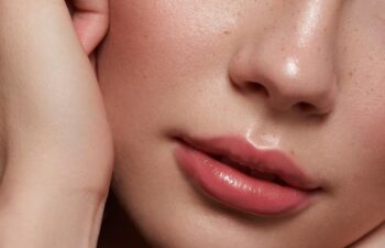 Close up of beautiful young woman's face with fresh, smooth skin and pink lips with light background _ Skin and body care