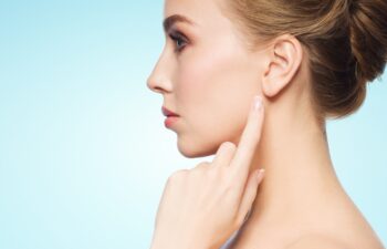 health, people and beauty concept - beautiful young woman pointing finger to her ear over blue background