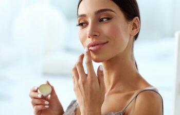 Lips Skin Care. Beautiful Woman With Beauty Face Applying Lip Balsam, Lipbalm On Full Sexy Lips. Portrait Of Smiling Female Model With Soft Skin And Natural Nude Makeup Touching Lips. High Resolution