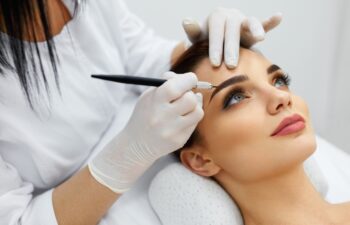 Permanent Makeup For Eyebrows. Closeup Of Beautiful Woman With Thick Brows In Beauty Salon. Beautician Doing Eyebrow Tattooing For Female Face. Beauty Procedure. High Resolution