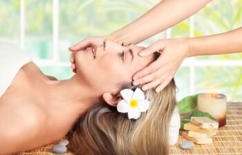 Beautiful blond woman lying down on massage table in spa salon, enjoying facial massage, doing facial mask, healthy lifestyle and beauty treatment concept