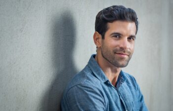 Handsome young man posing on grey background. Portrait of satisfied businessman against grey wall. Close up face of fashionable latin man on grey background.