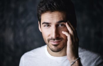 Portrait of a handsome smiling young man wearing white t-shirt. Studio shot over dark background. Men's beauty and health.