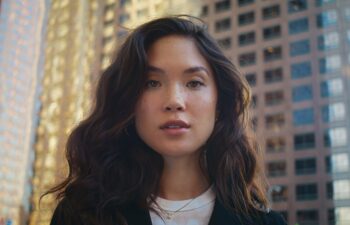 Portrait of beautiful asian woman standing near modern city skyscraper close up. Gorgeous brunette girl looking camera on sunlight. Attractive model posing on megapolis street on summer day closeup.