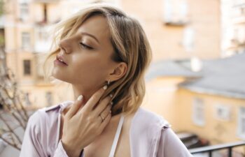 In profile close-up gentle image of young caucasian woman with languid look outdoors. Short-haired blonde tucked her hair behind ear, dressed in casual light clothes.